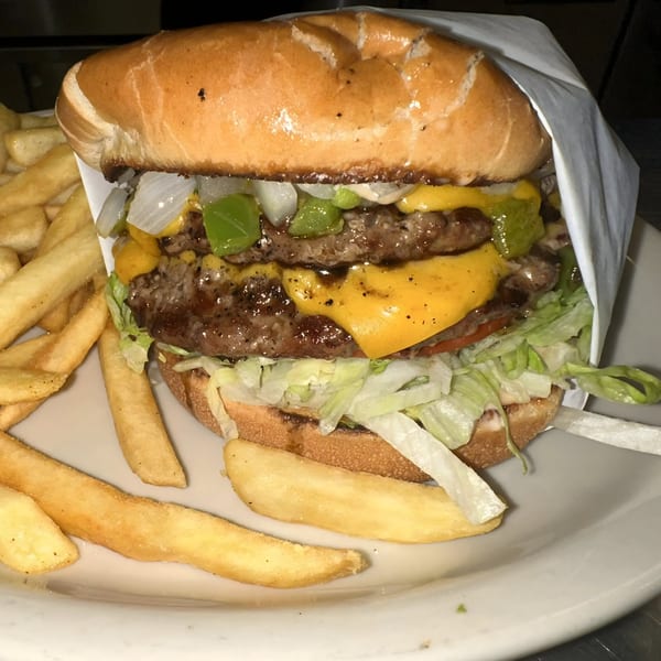 A double cheeseburger with lettuce, onions, and peppers, served with a side of fries.