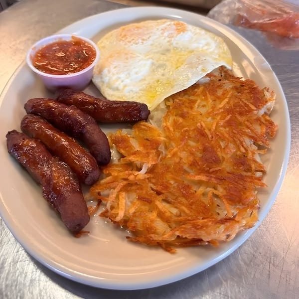 A breakfast plate with four sausages, hash browns, two fried eggs, and a side of salsa.