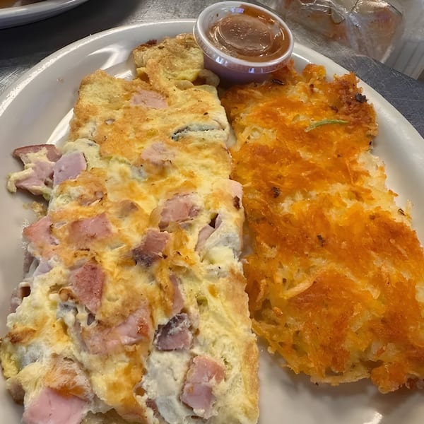 Ham and cheese omelet with a side of crispy hash browns and a small cup of sauce.