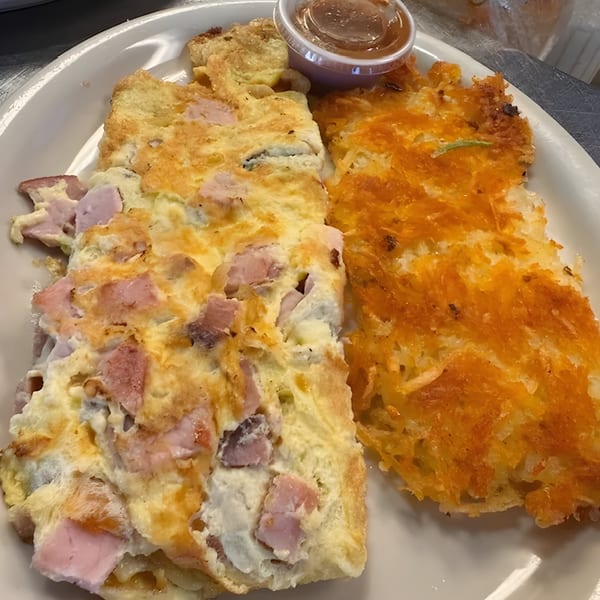 A ham and cheese omelet with a side of crispy hash browns and a small cup of sauce.