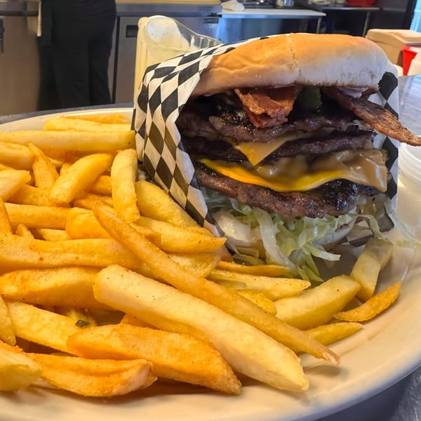 A large triple bacon cheeseburger with lettuce and a side of golden french fries on a white plate.