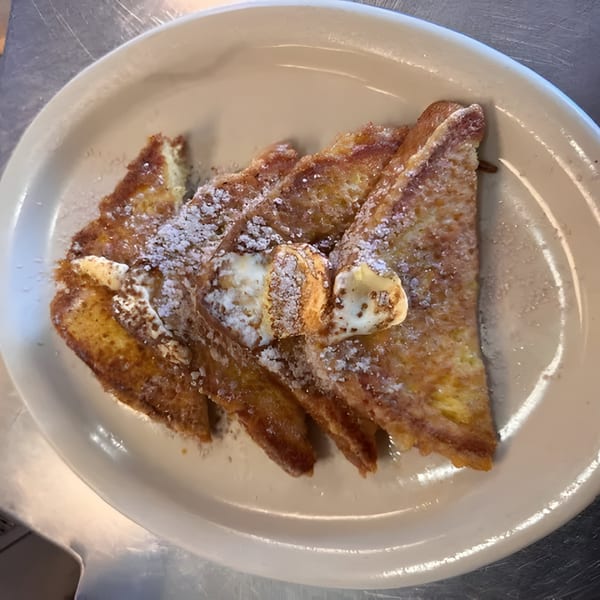 Golden French toast triangles with powdered sugar and butter pats on a white plate.